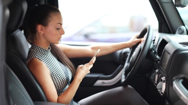 Frau schaut aufs Handy beim Fahren (Symbolbild)