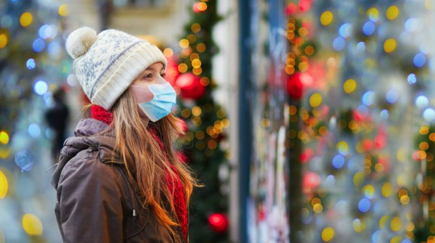 Frau mit Mund-Nasen-Bedeckung vor Weihnachtsbeleuchtung in Innenstadt.