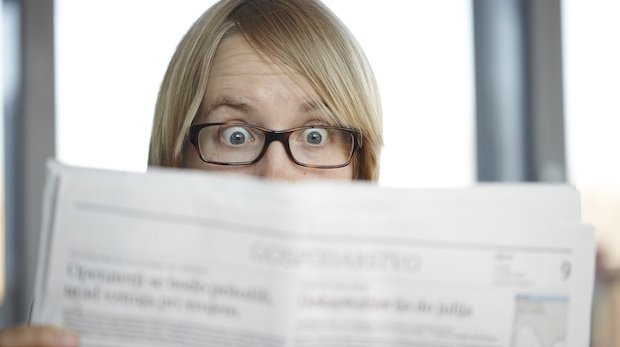 Frau mit schockiertem Gesichtsausdruck liest Zeitung