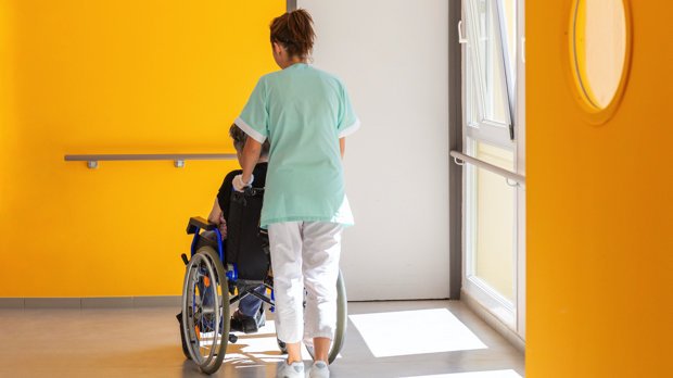Pflegekraft schiebt Person im Rollstuhl