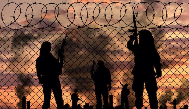 Silhouetten von Kämpfern der Terrororganisation Islamischer Staat an einem Grenzzaun