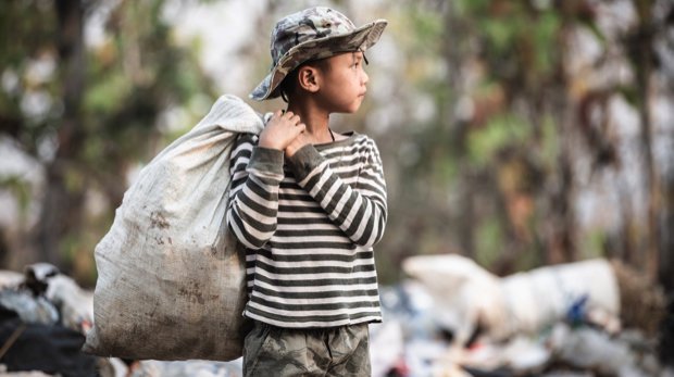 Kind mit schwerem Müllsack auf einer Müllhalde.