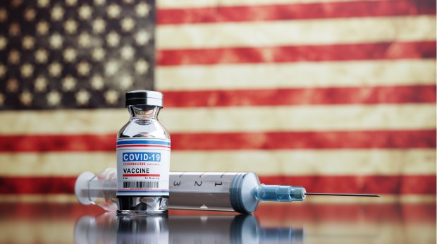 Eine Impfdose mit Spritze vor der US-amerikanischen Flagge
