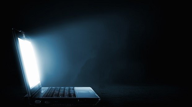 Laptop vor schwarzer Wand leuchtet