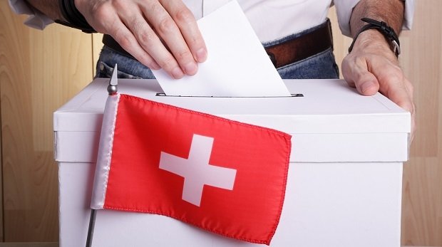 Mann wirft Umschlag in Wahlurne mit Schweizer Flagge