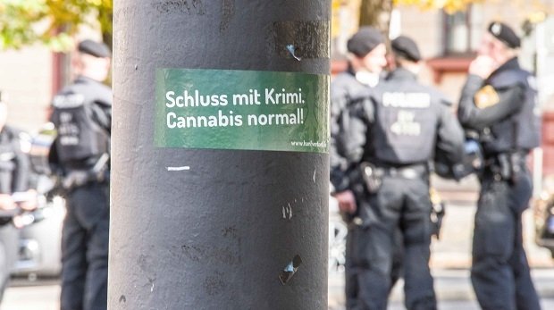 Ein Sticker mit der Aufschrift "Schluss mit Krimi. Cannabis normal!" an einer Laterne.