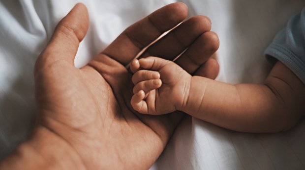 Die Hand eines Mannes, in der die Hand eines Babys liegt.