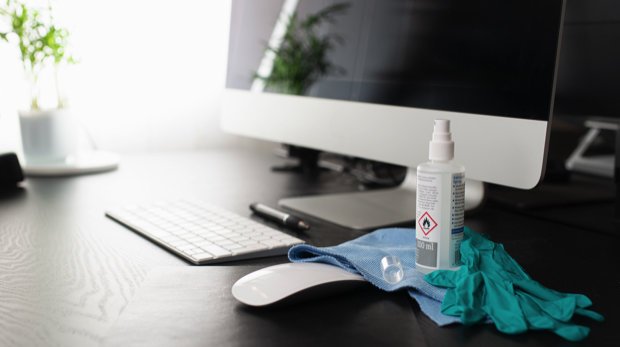 Verlassener Schreibtisch mit Computer, Desinfektionsmittel und Hygienehandschuhen