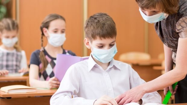 Schüler und Lehrerin mit Mund-Nasen-Schutz in der Schule.