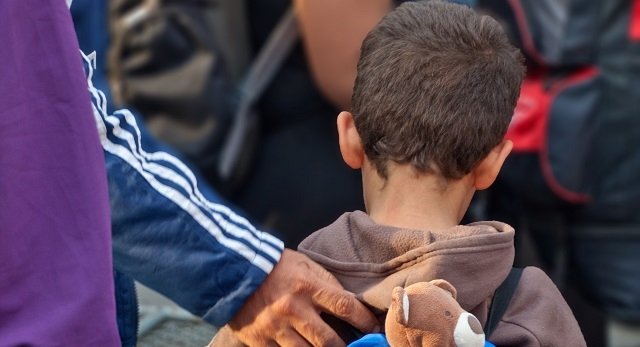 Flüchtlingkind mit Hand und Teddy am Rücken
