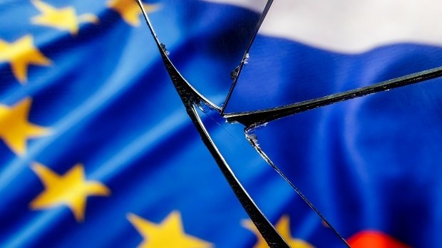 Flaggen von EU und Russland speigeln sich im zerbrochenen Glas.