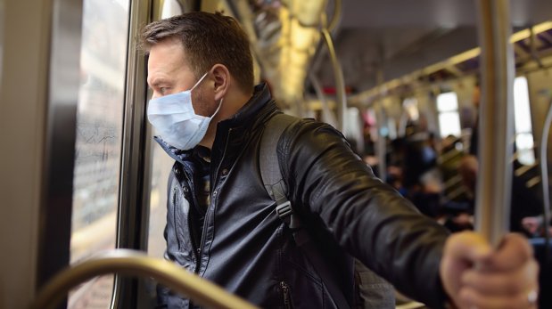 Mann mit Mund-Nasen-Bedeckung im öffentlichen Verkehrsmittel (Symbolbild)