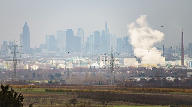 Im Dunst liegt die Skyline von Frankfurt am Main hinter den Anlagen des Industrieparks im Stadtteil Höchst (u) beim Blick von einem Hang im nahegelegen Kriftel.