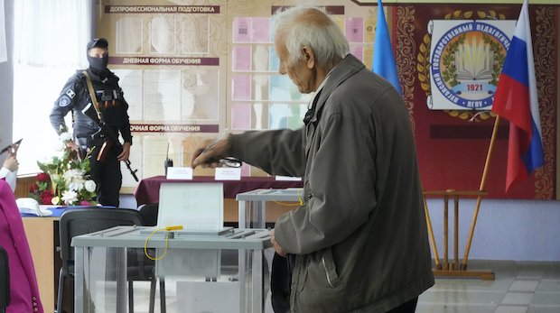 Ein Mann gibt am 27. September 2022 seine Stimme für das Referendum in Luhansk ab, bewacht von einem bewaffneten Separatisten.