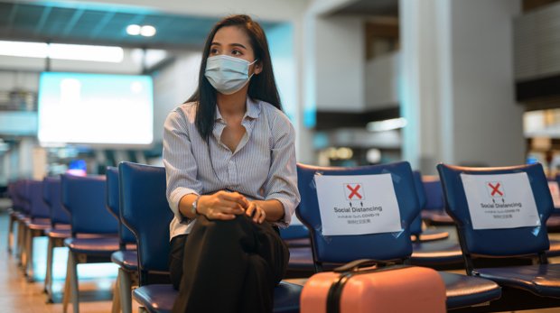 Touristin mit Mund-Nasen-Schutz am leeren Flughafen
