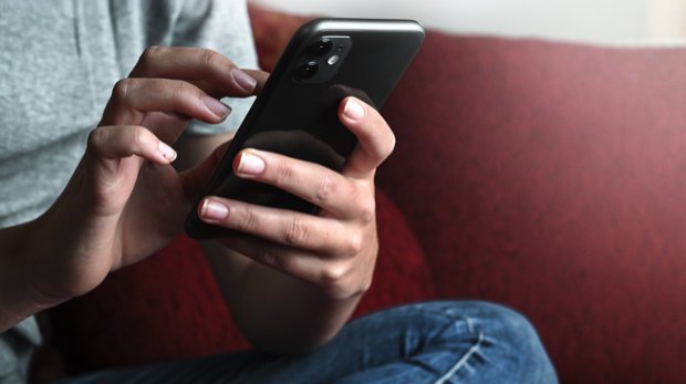 Handynutzer mit Smartphone auf einem roten Sofa