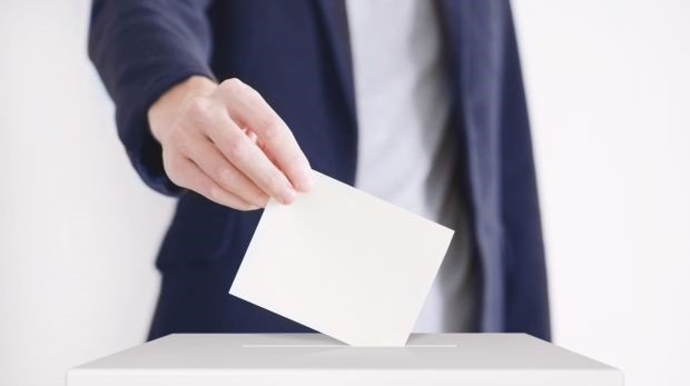Mann im Anzug wirft Wahlzettel in Wahlurne