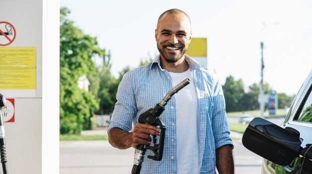 Lachender Mann mit einer Zapfpistole an einer Tankstelle