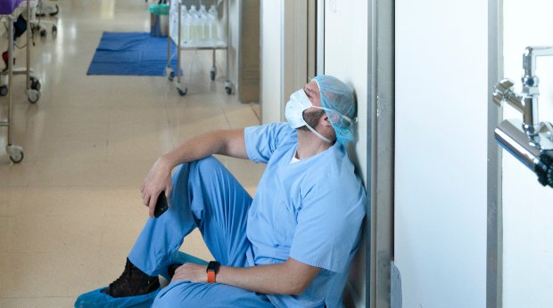 Ein Krankenpfleger sitzt müde in einem Krankenhaus auf dem Flur