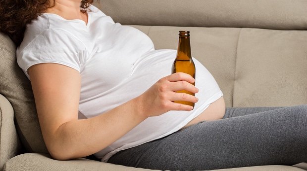 Schwangere mit Bier auf Sofa