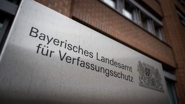 in Metallschild mit der Aufschrift "Bayerisches Landesamt für Verfassungsschutz" steht vor dem Gebäude der Einrichtung.