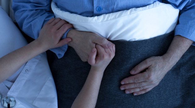 Eine Ärztin hält die Hände einer im Bett liegenden Person im Krankenhaus