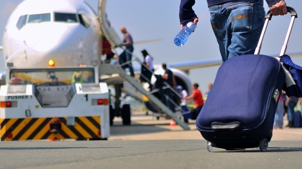 Mann mit Koffer auf Rollfeld vor einem Flugzeug