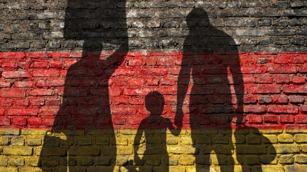 Schatten von drei Personen auf Wand mit Farben der deutschen Flagge.