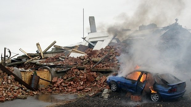 Ein zerstörtes Gebäude nebst brennendem Kleinwagen