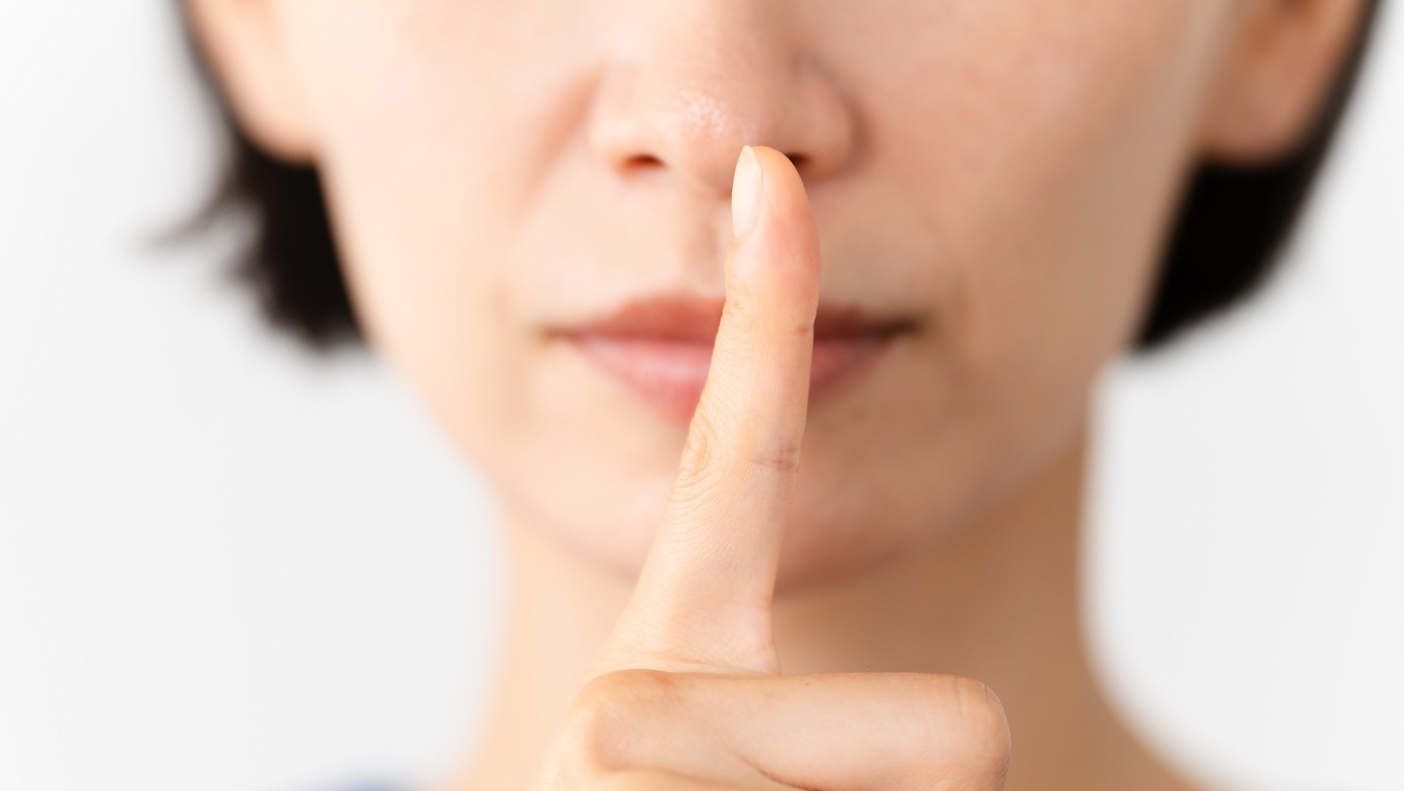 Frau macht die Schweigegeste mit Finger über dem Mund.