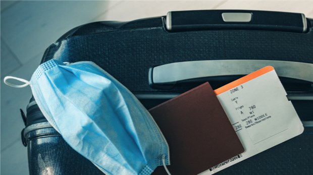 Koffer mit Reisepass, Flugticket und Mund-Nasen-Schutz