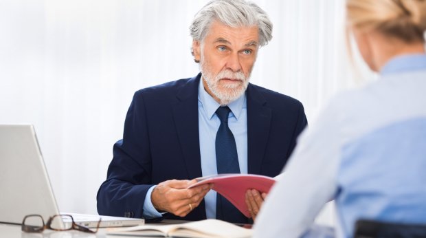 Ein älterer Mann, am Schreibtisch sitzend, spricht mit einer anderen Person