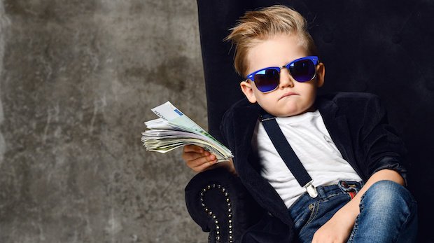 Rich kid: Junge mit Sonnenbrille in einem Sessel und Geldbündel in der Hand.