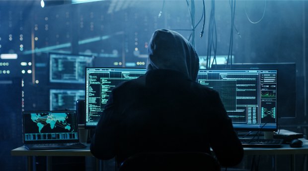 Eine Person mit Kapuze sitzt im Dunkeln am Computer