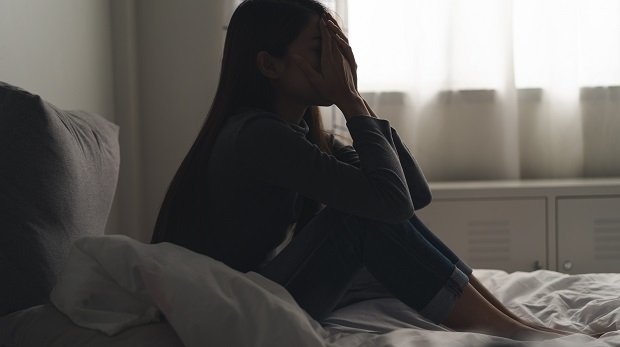 Eine Frau mit Depressionen sitzt in einem Bett (Symbolbild)