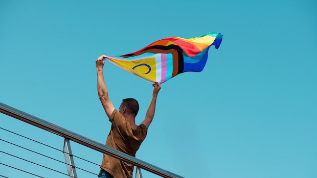 Ein Mensch hält die "Progress Pride"-Fahne hoch.