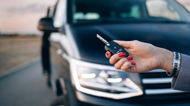 Frau hält Autoschlüssel vor einem Minivan in der Hand