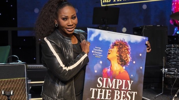 Dorothea "Coco" Fletcher steht auf einer Bühne und hält ein Plakat ihrer Show "Simply The Best - Die Tina Turner Story"