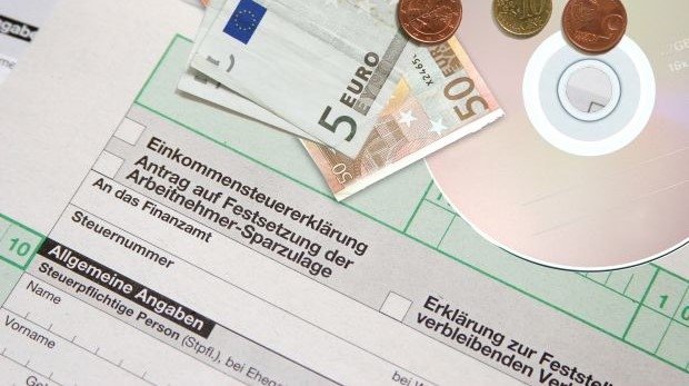 Münzen, Scheine und eine CD liegen auf einem Formblatt der Einkommensteuererklärung
