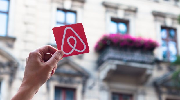 Airbnb Logo vor einem Haus mit Mietwohnungen
