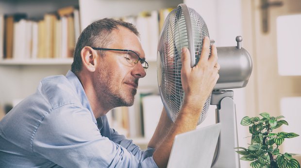Ein verschwitzter Mann sucht Kühlung durch einen Ventilator
