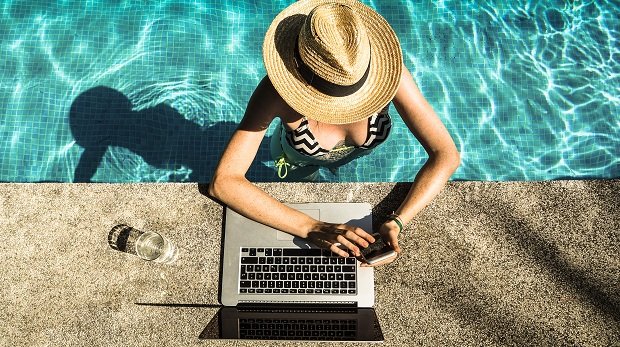 Eine Frau im Pool nutzt Computer und Smartphone (Symbolbild)