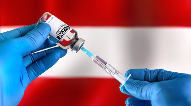 Behandschuhte Hände ziehen eine Spritze mit Impfstoff vor der österreichischen Flagge auf