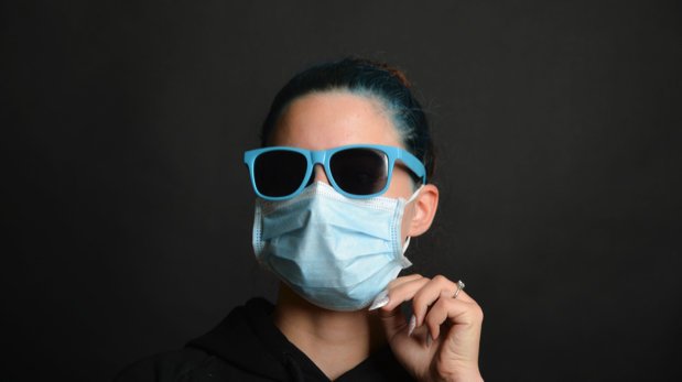 Junge Frau mit Mund-Nasen-Bedeckung und Sonnenbrille.