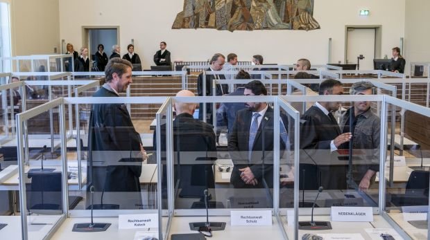 23.04.2020, Rheinland-Pfalz, Koblenz: Nebenkläger stehen vor Prozessbeginn neben Anwälten im Gerichtssaal des Oberlandesgerichts zwischen Corona-Schutzscheiben.