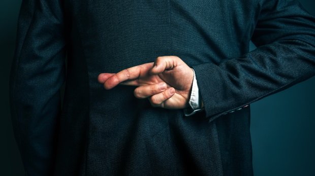 Mann im Anzug kreuzt Finger hinterm Rücken (Symbolbild)