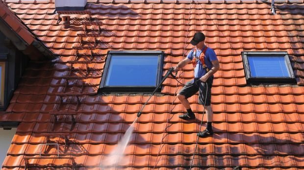 Mann behandelt Dach mit einem Hochdruckreiniger (Symbol)