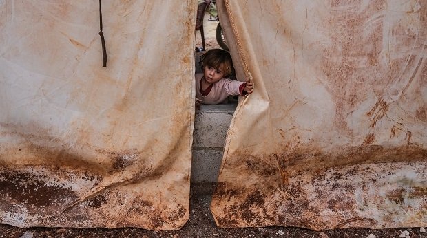 Ein Mädchen in Syrien schaut aus einem Zelt heraus