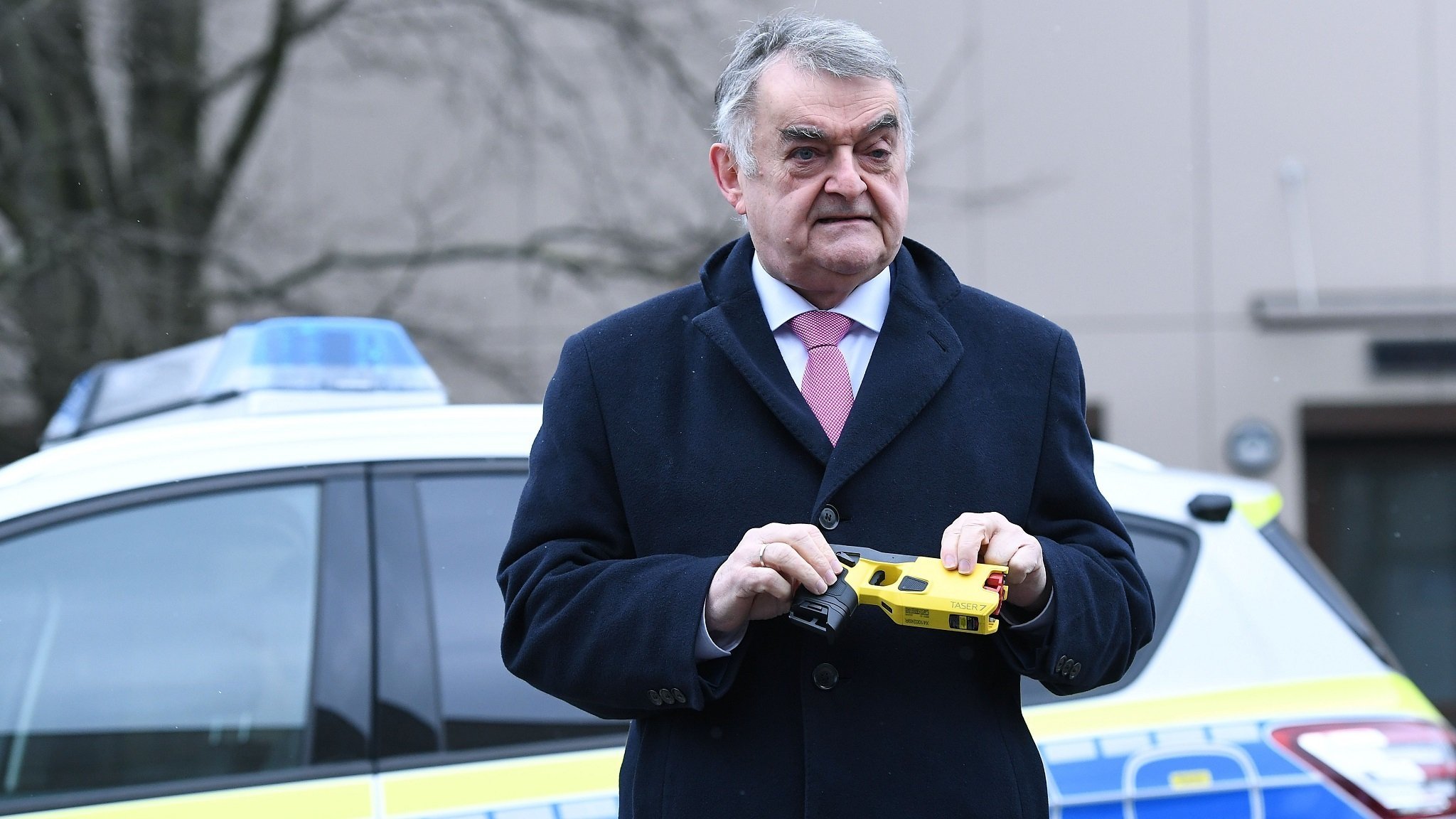 Innenminister Reul mit Elektroschocker in der Hand vor Polizeifahrzeug