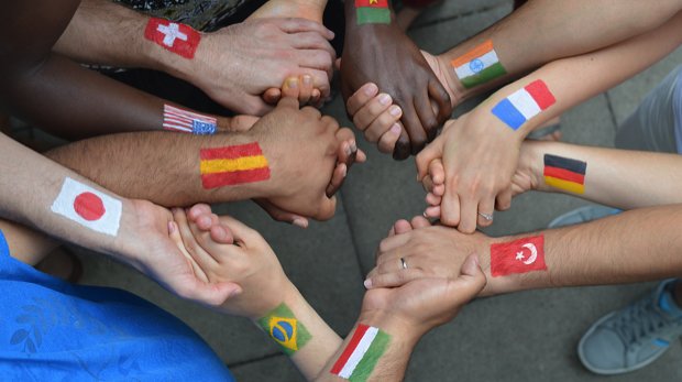 Viele Hände halten sich gegeneinander fest. Nationalflaggen sind auf die Arme gemalt.